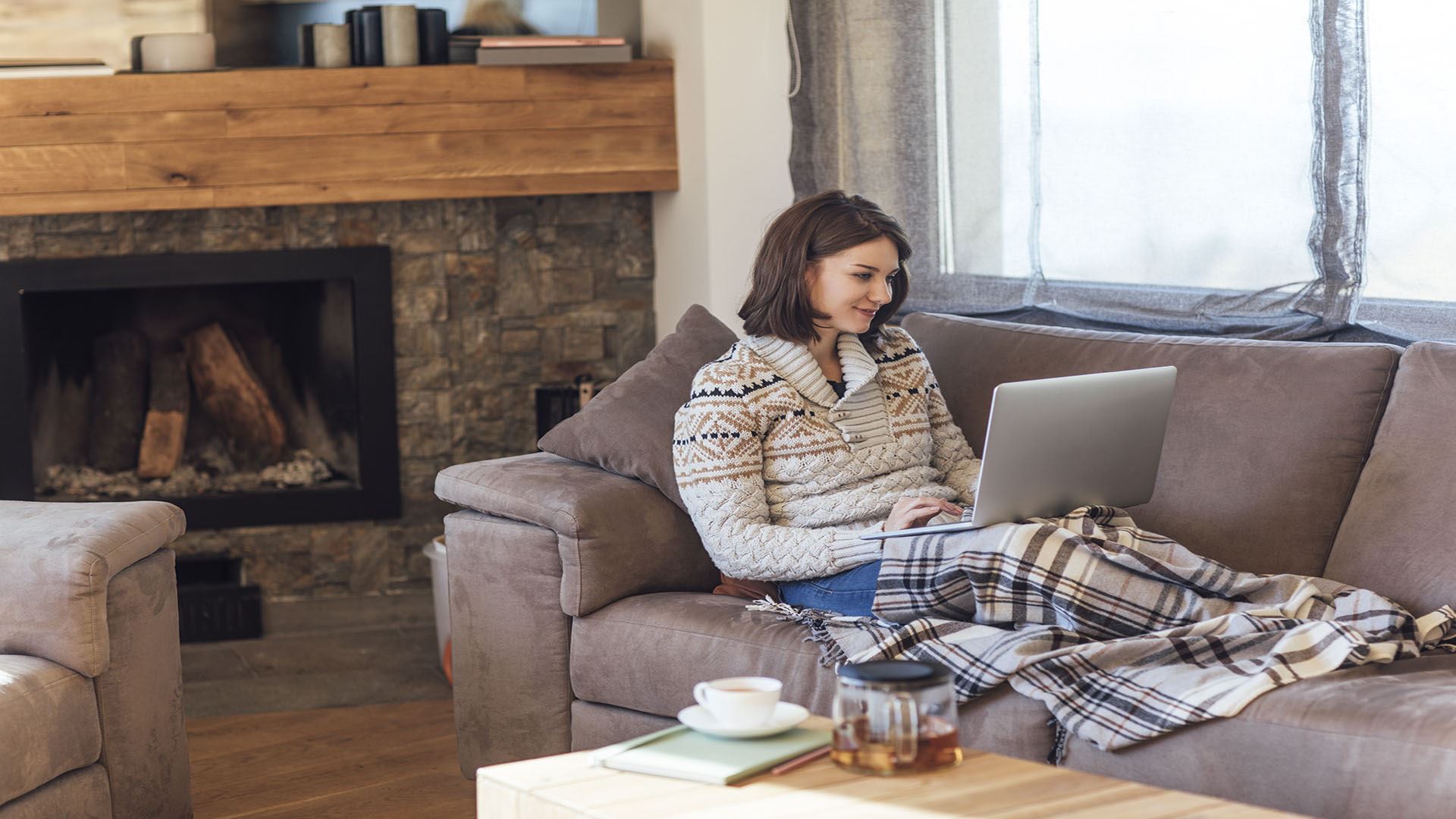 Woman sitting on couch under a blanket working on a laptop