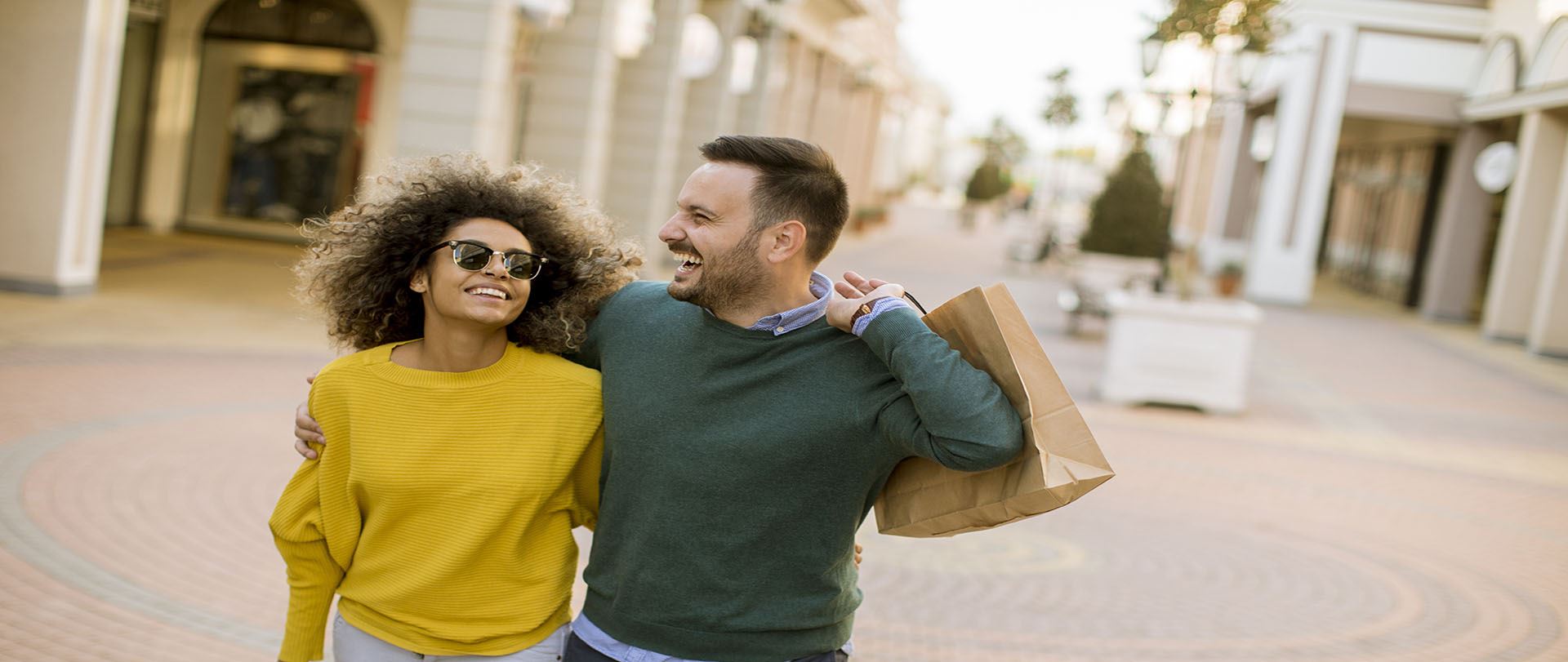 Man and woman walking through a shopping mall with a bag, both are smiling