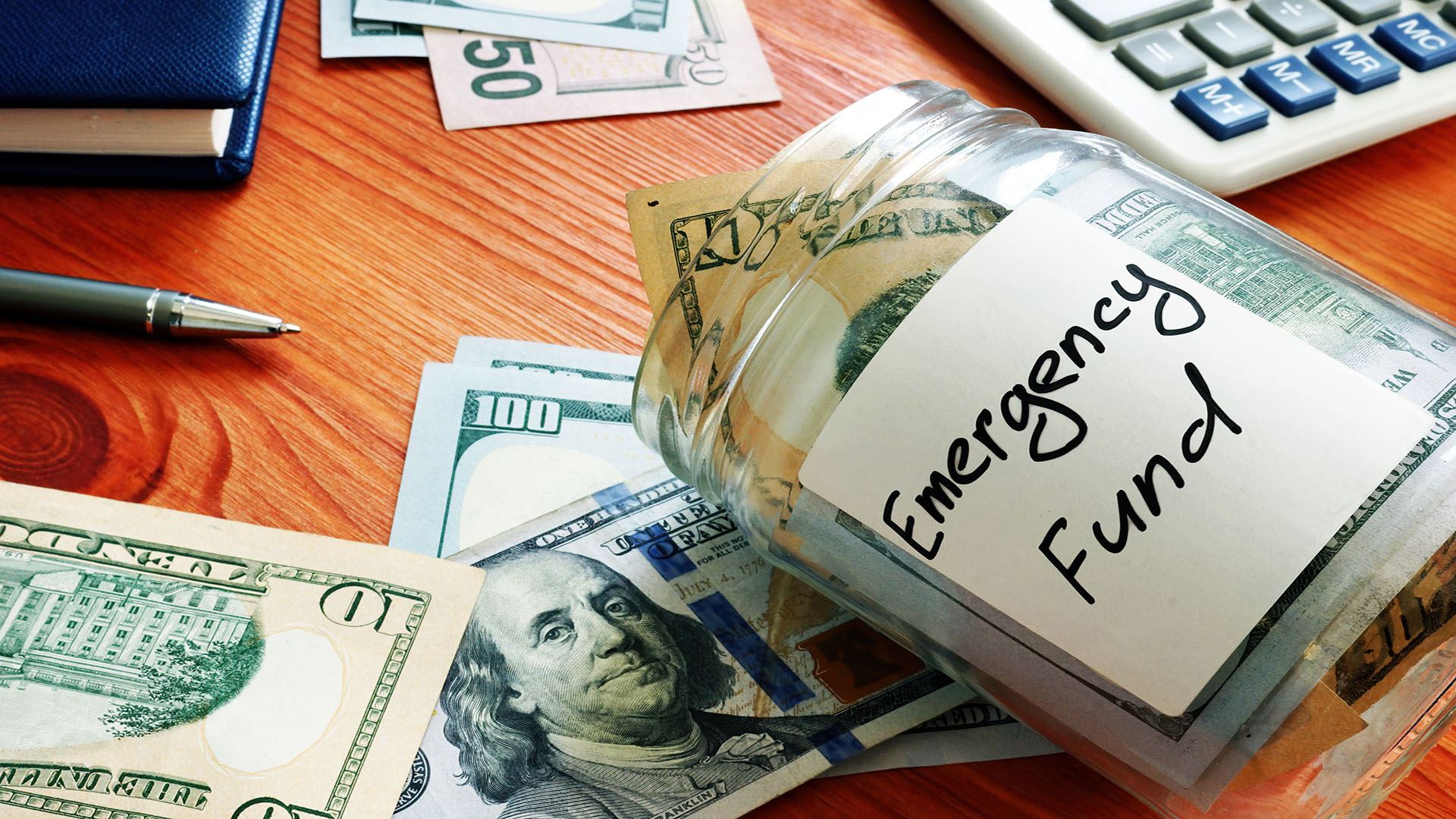 money laying on a table with a jar marked emergency fund